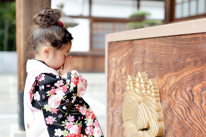 着物を着て神社の境内の前でお祈りをする女の子