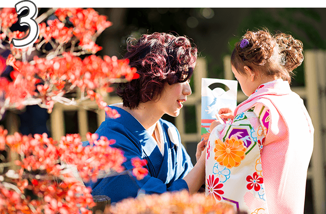 紅葉を背景に、着物を着たお母さんと千歳飴を持つ3歳の女の子の写真
