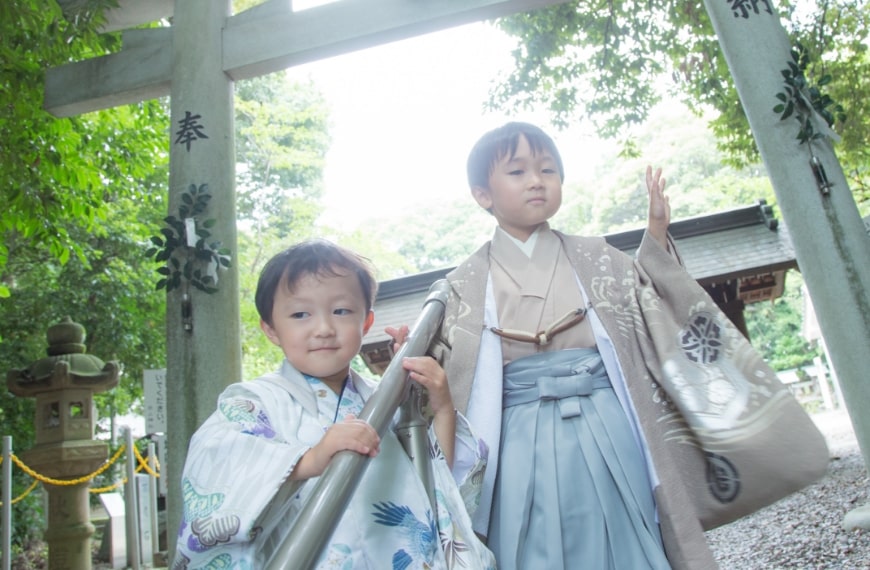 神社の鳥居の下で、七五三の着物と袴を着た二人の男の子が立っている様子